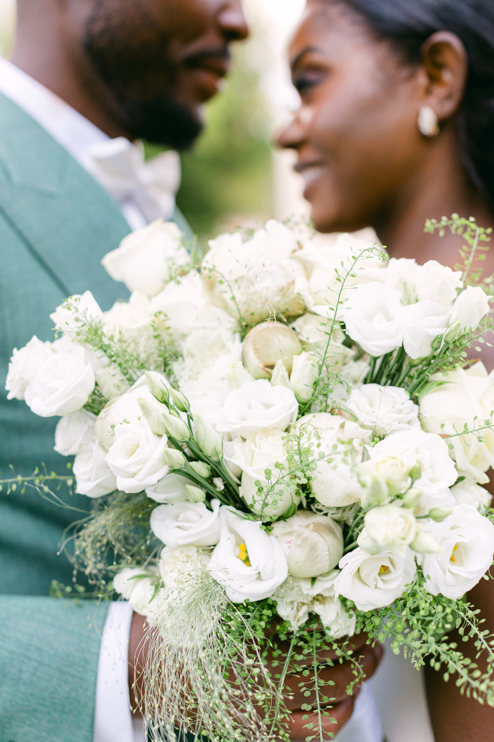 Bouquet de mariée blanc au premier plan, couple en arrière-plan flou